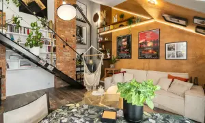 Salon w stylu loftowym z ceglaną ścianą, metalowymi schodami, wiszącym fotelem i wygodną kanapą.
