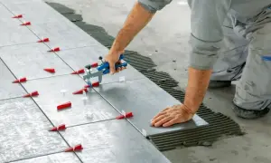 Instalator pokazuje, jak kłaść płytki na podłodze, używając poziomicy i klina do precyzyjnego układania.