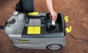 Ręka dodaje środek czyszczący do odkurzacza piorącego Karcher Puzzi 10/2. Dowiedz się, karcher rm 760 jak stosować, by skutecznie wyczyścić dywan.