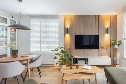 Przytulny salon inspiracje: drewniana ściana z TV, jadalnia, rośliny i wygodna sofa tworzą ciepłą atmosferę.