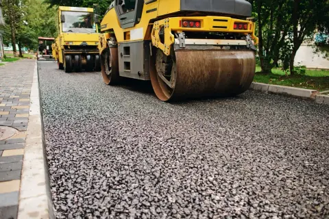 Walec drogowy wyrównuje świeżo położony asfalt. Pospółka drogowa czeka na kolejne warstwy.