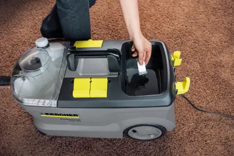 Ręka dodaje środek czyszczący do odkurzacza piorącego Karcher Puzzi 10/2. Dowiedz się, karcher rm 760 jak stosować, by skutecznie wyczyścić dywan.