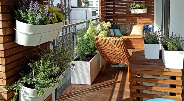 Jak urządzić mały wąski balkon w bloku inspiracje: zielone ściany, wygodne siedzisko i rattanowy fotel tworzą przytulną oazę.