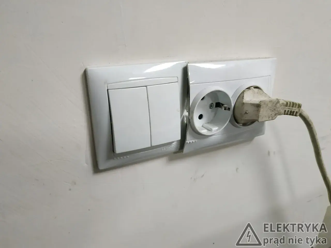 Biały montaż: włącznik światła i gniazdko elektryczne z wtyczką. Na ścianie widoczny znak ostrzegawczy "Elektryka prąd nie tyka".