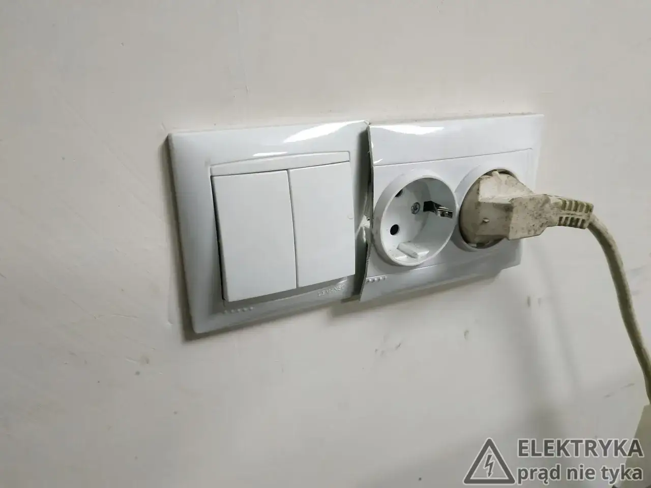 Biały montaż: włącznik światła i gniazdko elektryczne z wtyczką. Widać pęknięcie na obudowie.