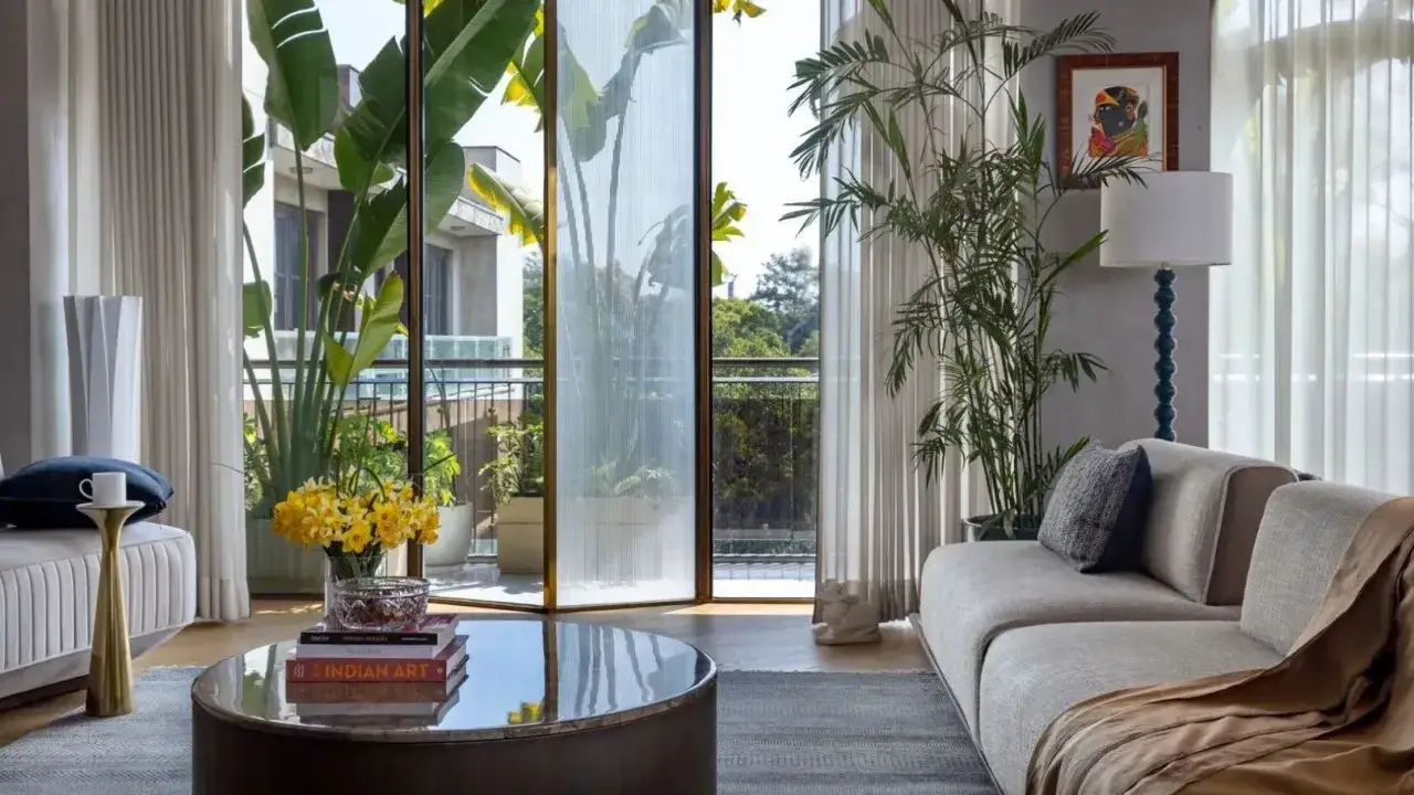 Jasny salon z sofą, stolikiem kawowym i bujną roślinnością wychodzącą na balkon. Wnęka balkonowa pełna zieleni tworzy przytulną atmosferę.