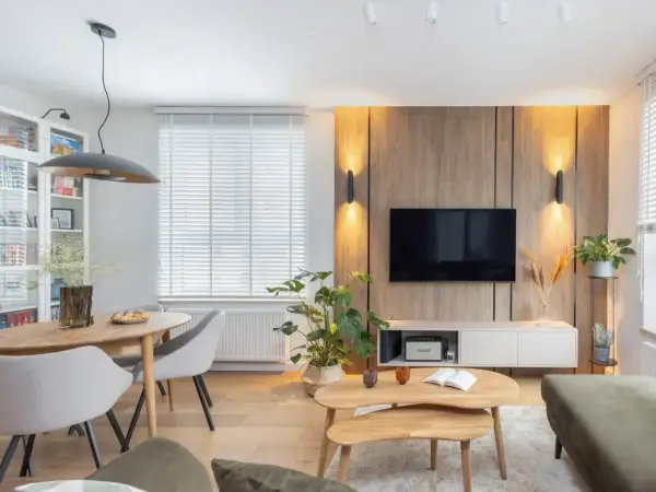 Przytulny salon inspiracje: drewniana ściana z TV, jadalnia, rośliny i wygodna sofa tworzą ciepłą atmosferę.